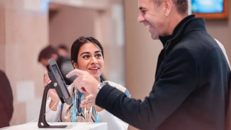 A man and a woman laughing together in front of a monitor at a registration counter.
