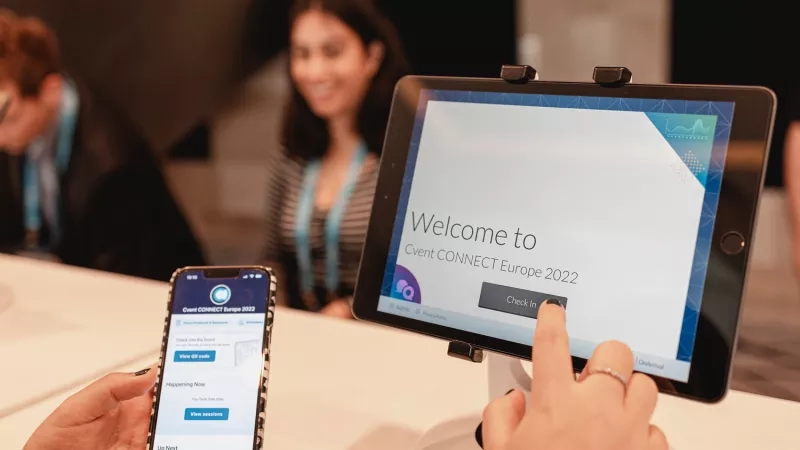 A person touches a tablet displaying "Welcome to Event Connect Europe 2022" while holding a smartphone.