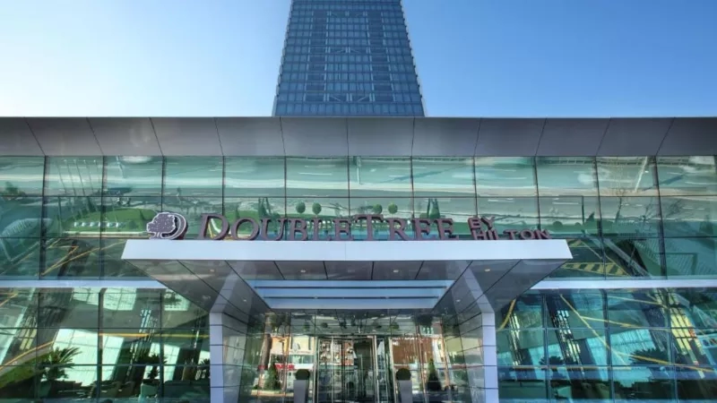 Exterior view of DoubleTree by Hilton Hotel Izmit with a glass facade, modern architecture, and lush landscaping.