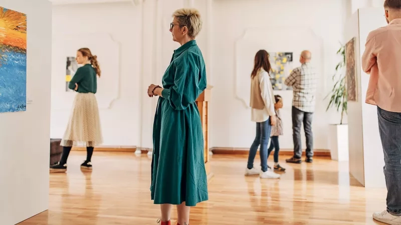 People in an art museum standing around paintings on the walls and talking to each other.