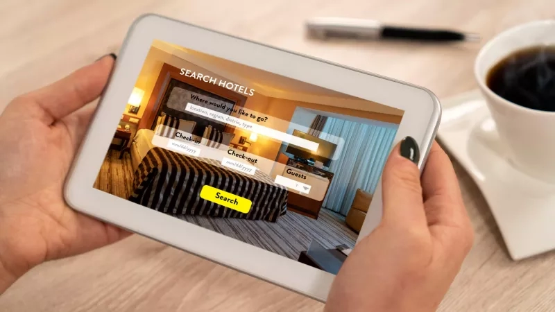 Person holding a tablet showing a hotel booking website with a cup of coffee next to it.