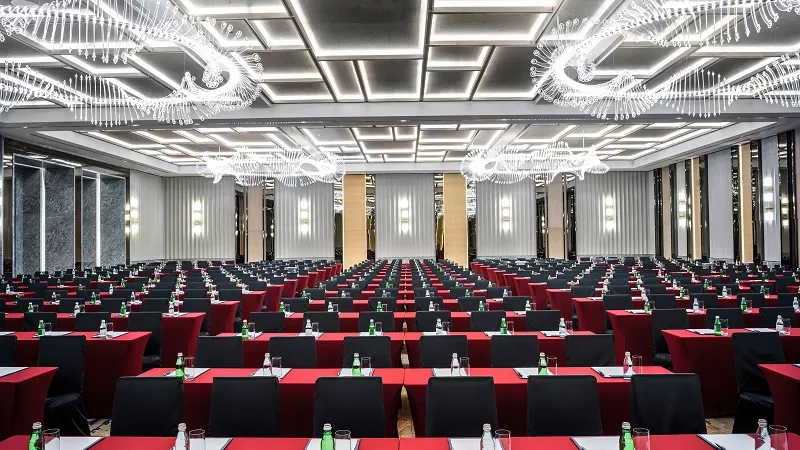ICPQ ballroom in classroom setup with desks and chairs, two bottles per desk, and chandeliers hanging above.