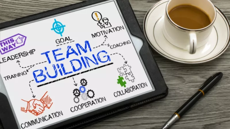 Tablet with a team building drawing and a cup of coffee next to it on a wooden table.