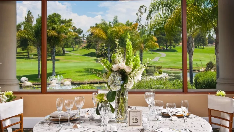 An event at a country club with a golf course view, featuring dining setup and floral arrangements.