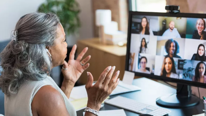 Woman attending a virtual corporate event in an office with a computer and people on the screen.