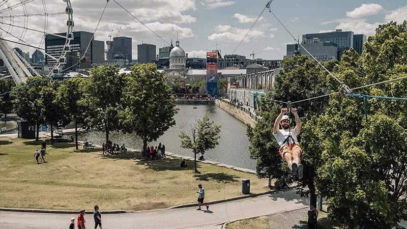 A man is riding a zipline in the air while the cityscape is in the background.