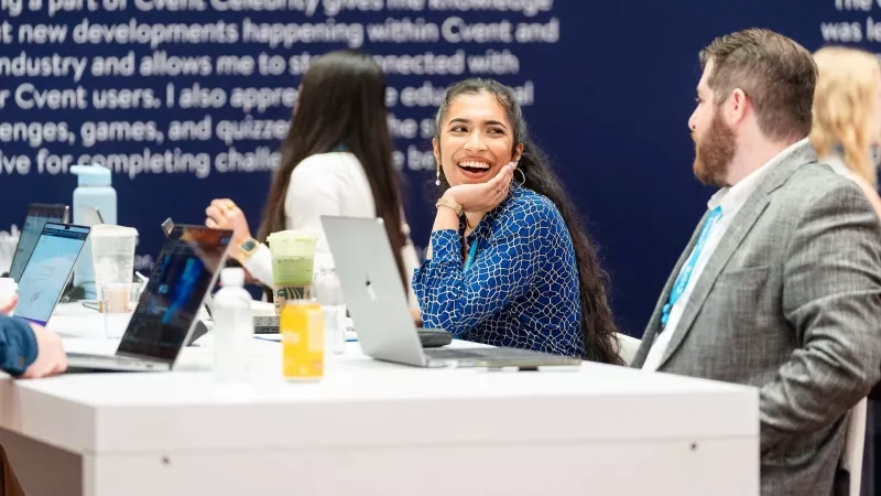 Cvent CONNECT 2023 attendees work together at a Kickoff Meeting table with laptops, drinks, and snacks.