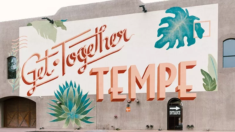 Get Together Tempe is written on a beige building wall with green leaves and a black door on the side.