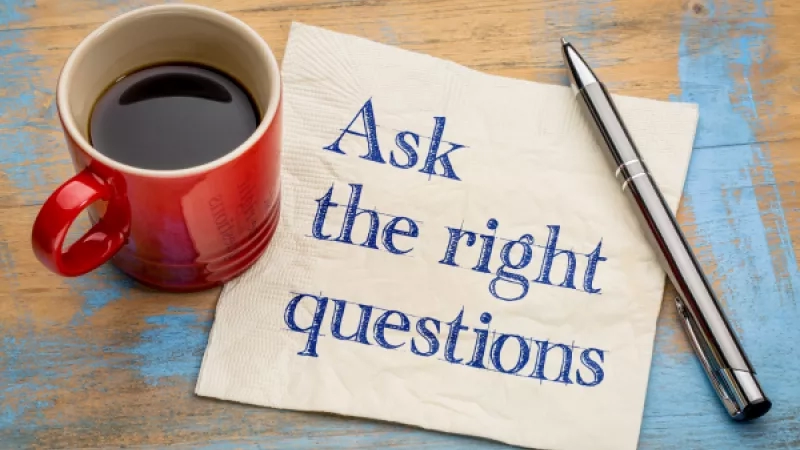 A cup of coffee, pen, and napkin with "Ask the right questions" written on it.