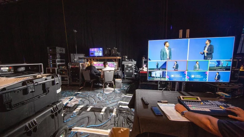 Production room for virtual event with video board showing two speakers on split screen and crew at consoles.
