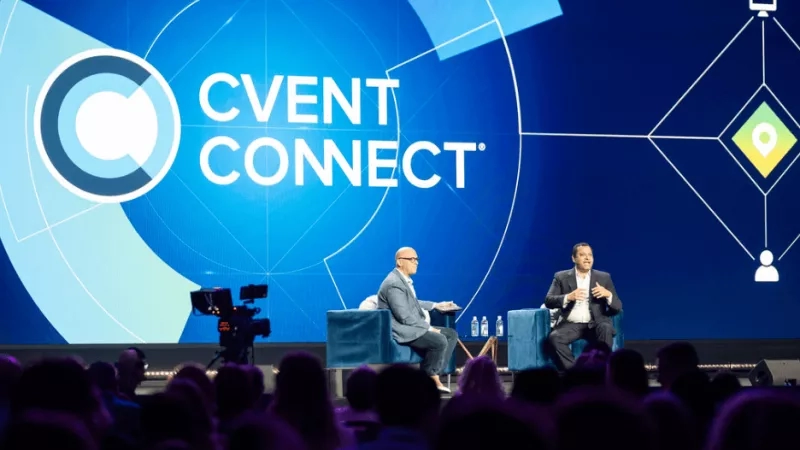 Two men sit on stage at the Cvent Connect conference with a large screen behind them.