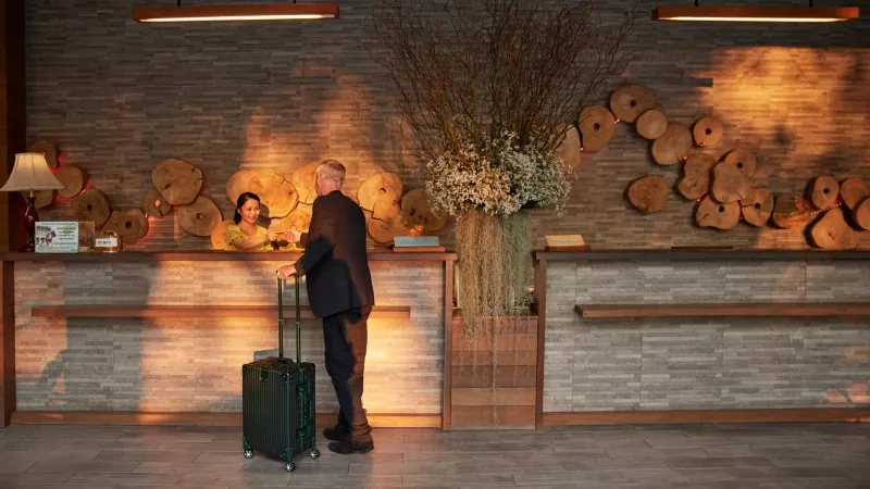 Man with a suitcase at the reception desk at a hotel lobby.