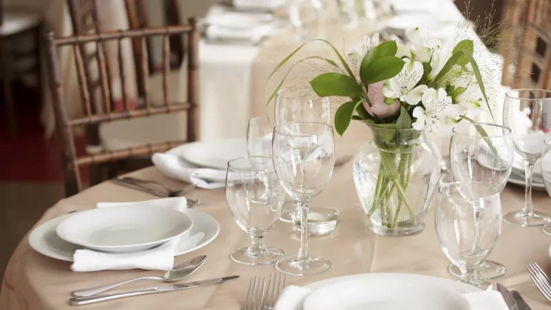 Hotel wedding reception set up with white plates, napkins, and flowers on each table.
