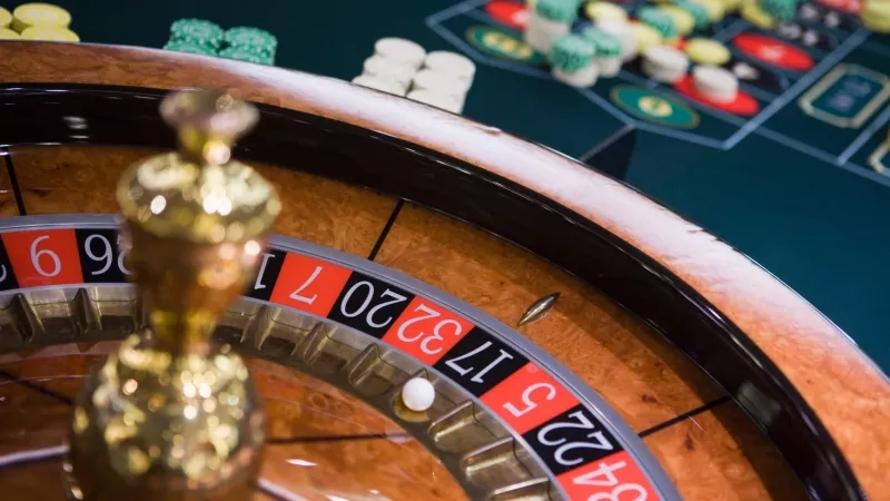 A closeup of a roulette wheel with chips and a table in the background.