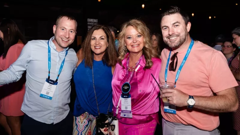 A group of four people in pink and blue attire are smiling for a photo at an event.