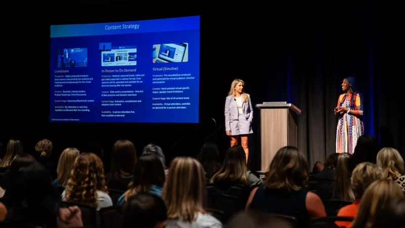 Two women stand on stage in front of an audience, with a screen displaying "Content Strategy" behind them.