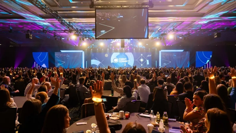A large crowd of people at an event in a large room with blue and purple lighting.