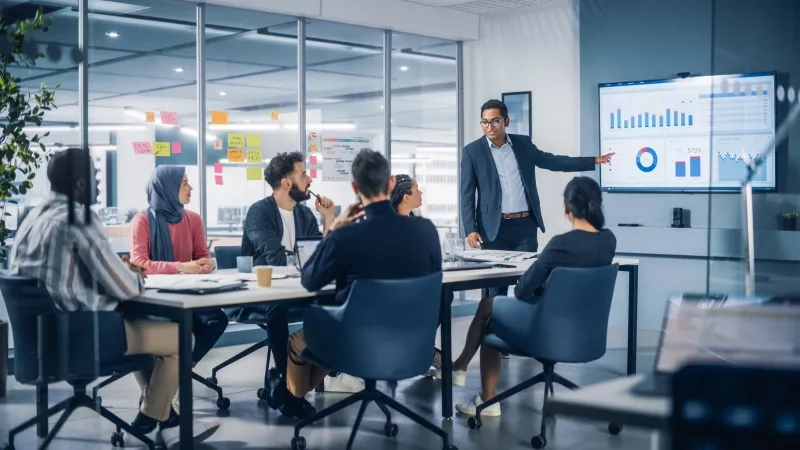 A group of people having a meeting in a modern office with a large screen in the background.
