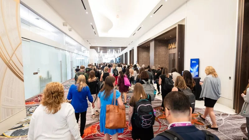 Large group of people walking down a hallway with a monitor displaying the Cvent Connect logo.