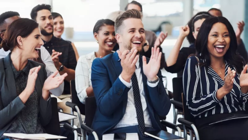 A group of people are seated in a row, clapping their hands and smiling at each other.