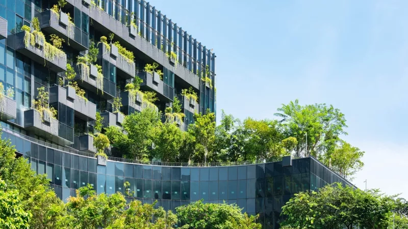 Green hotel with vertical urban garden and trees against a blue sky.