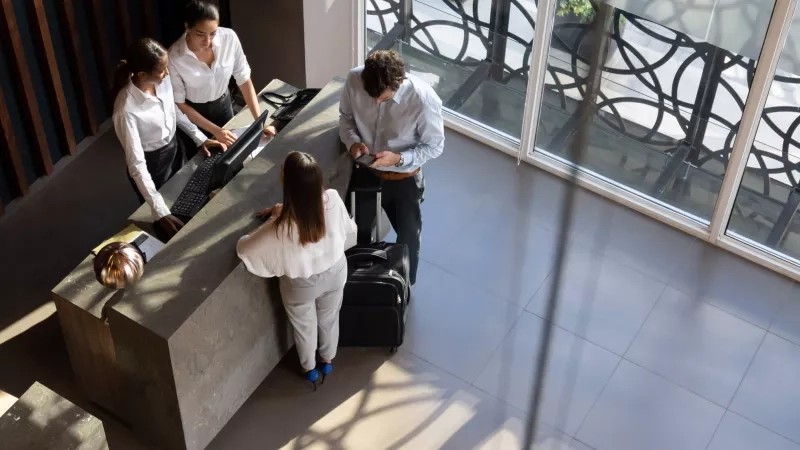 A hotel receptionist assisting a guest with a suitcase at the front desk.