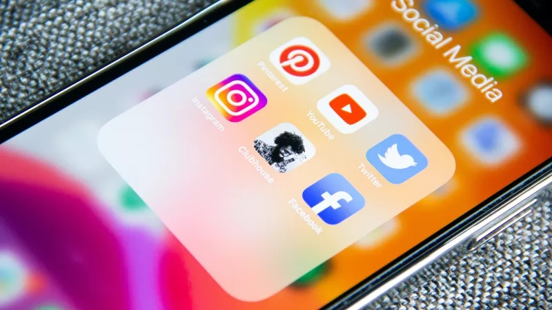 A smartphone screen displays the social media app icons for Instagram, Pinterest, Clubhouse, YouTube, Twitter, and Facebook.