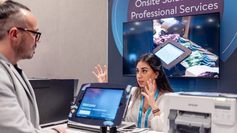 Epson employee talking to customer at a booth with a sign that says "Onsite Solutions & Professional Services."