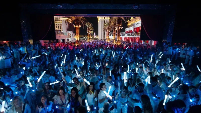 A crowd of people at a night event with a stage and palm trees in the background.