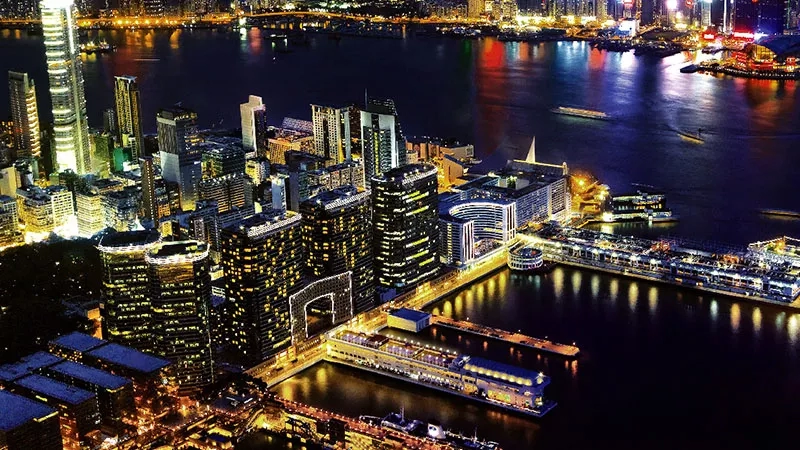 Harbour view of Marco Polo Hong Kong at night with boats, skyscrapers, and city lights.
