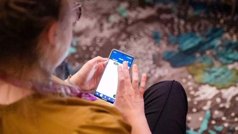 A woman sits on a carpet and uses the Cvent Event Planning App on her smartphone.