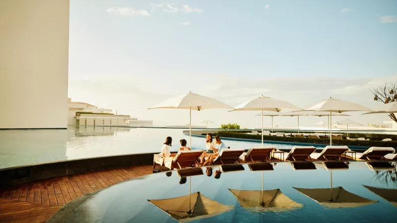 Outdoor pool area with umbrellas and lounge chairs under a clear sky at a luxury hotel.