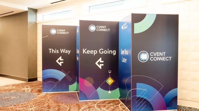 Three Cvent Connect event marketing posters in a hallway with a carpeted floor and beige walls.