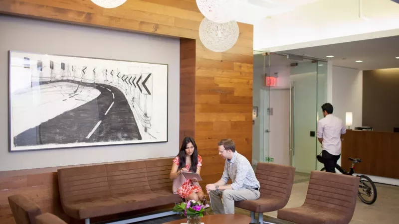 Two people are sitting on a bench and talking in the hotel lobby of the Graduate Ann Arbor.