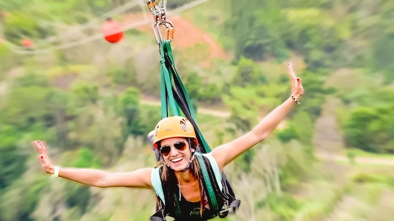 A woman is riding a zipline in Maui with both arms up and a smile on her face.