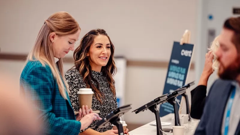 Two women and a man at a desk with digital screens and a sign reading "event."
