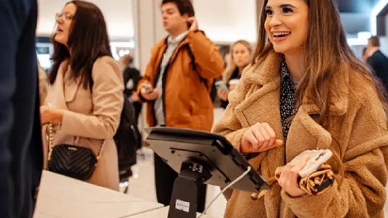 A woman with a brown fur coat is smiling while standing next to a monitor.