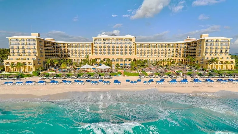 Aerial view of Paradisus Grand Cana resort, turquoise ocean, and blue beach chairs.