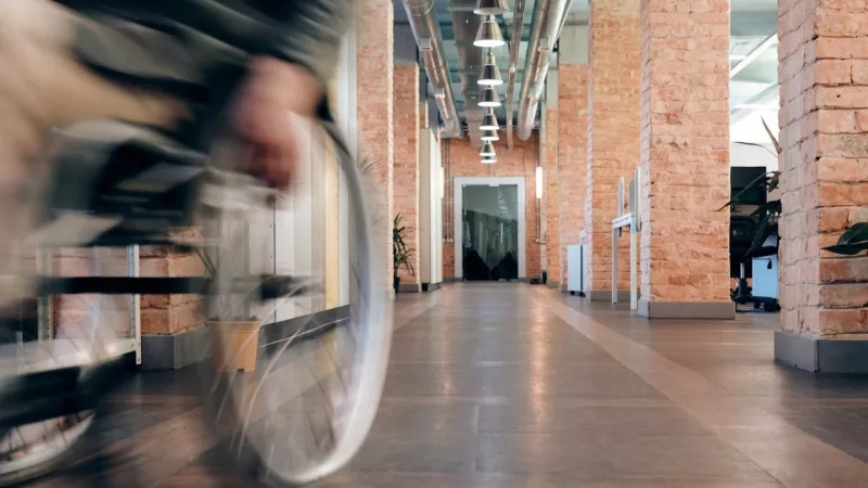 Blurry photo of a person in a wheelchair inside a hallway of a brick building.