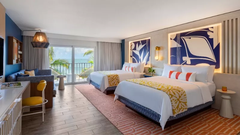 A two-bed guest room with a view of the ocean in the background.