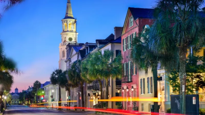 A blurred street with a church and trees in Charleston, SC, at dusk.