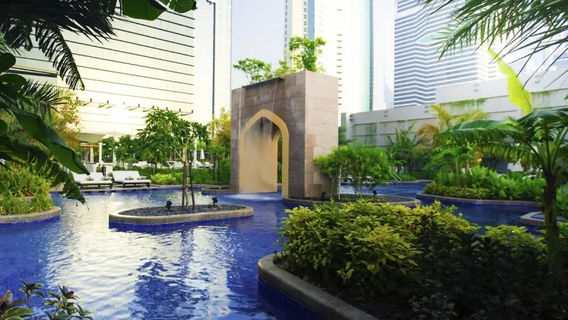 A beautiful pool with trees, a fountain, and buildings in the background, creating a peaceful atmosphere.