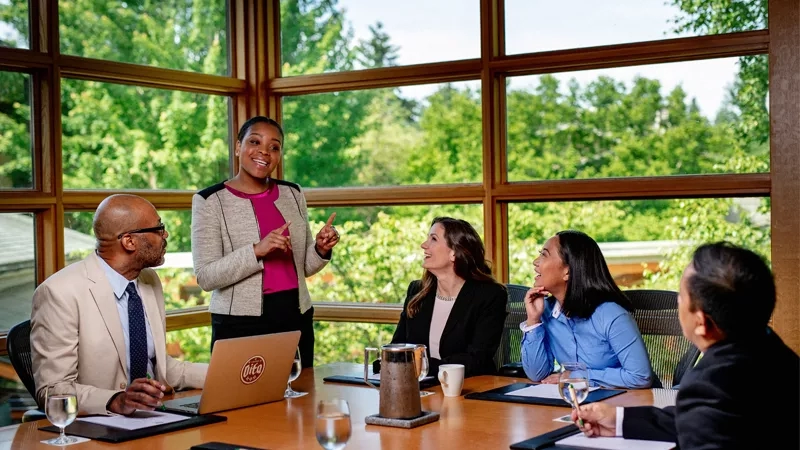 Five business professionals at a meeting with a woman leading the discussion.