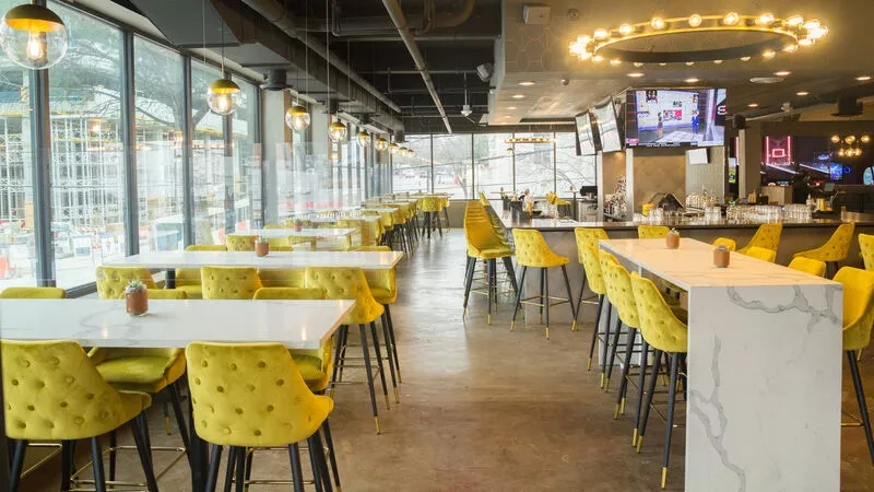 Interior of Bull and Bowl with yellow chairs, white tables, and large windows showing construction outside.