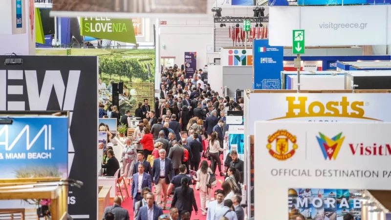 Visitors walk around the IMEX America 2023 trade show floor, passing stands and advertisements for various destinations.
