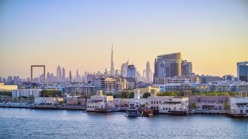 View of Dubai skyline with waterfront and boats on the water during sunset in the UAE.