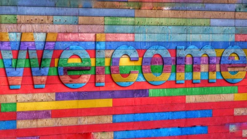 Wooden sign that says "Welcome" in large letters in front of colorful wood slats.