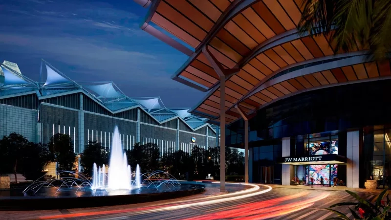 A night view of JW Marriott hotel entrance with a fountain, lights, and trees in Singapore.