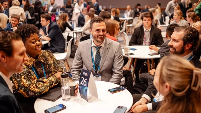 A group of people engaged in conversation at a round table with the number 26 on it.
