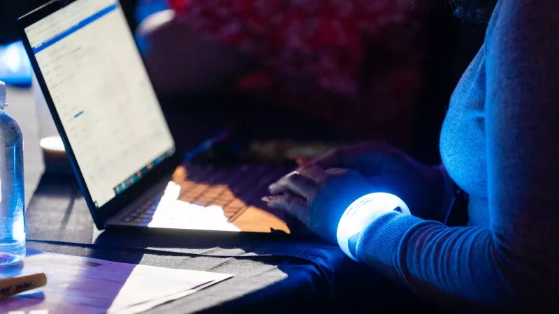 A person is typing on a laptop, with a bright glow on their hand from a bracelet.